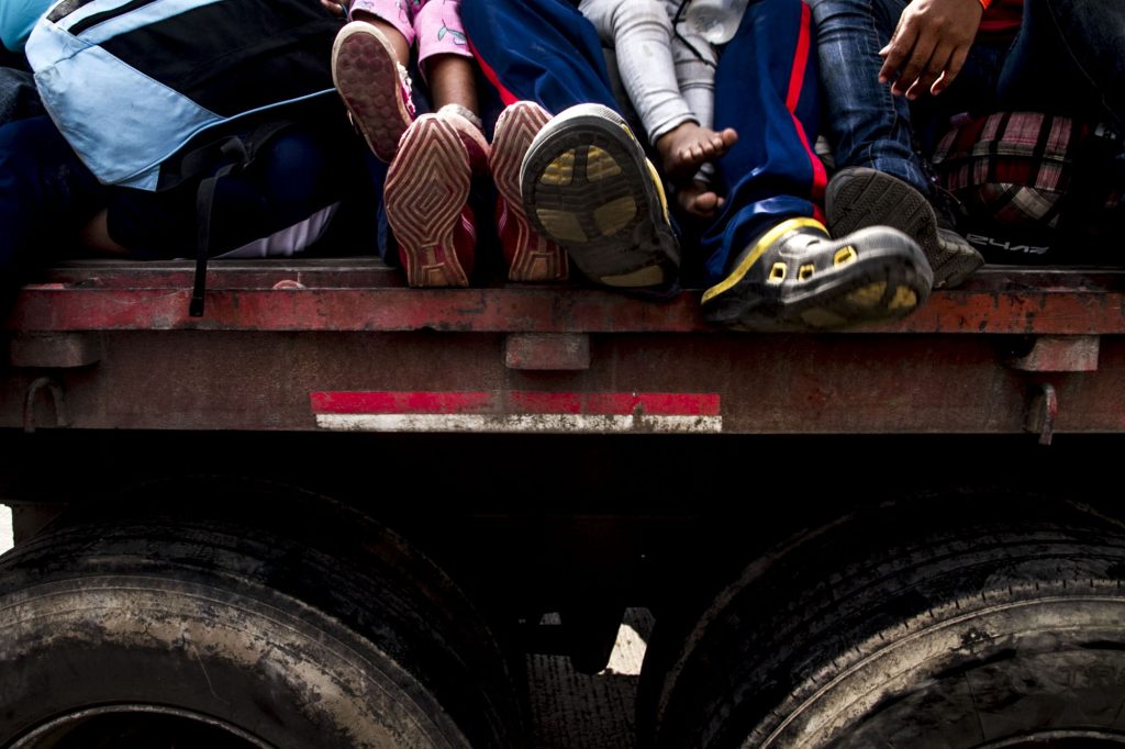 Tepotzotlán, State of Mexico. A barefoot girl amidst several migrants with feet protruding from the truck that will be giving them a ride on their journey. Photograph: Ernesto Álvarez.